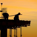 A construction worker is sitting on top of the building.