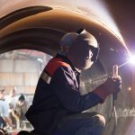 A man in a hard hat welding a pipe.