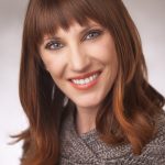 A woman with long hair and bangs smiles for the camera.