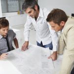 Three men are looking at a plan on the table.