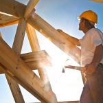 A man in yellow hard hat working on wooden structure.