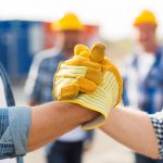 Two men in hard hats and gloves holding hands.