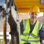 A man in yellow vest standing next to a construction vehicle.