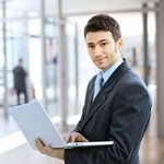 A man in suit and tie holding a laptop.