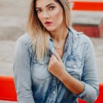 Woman in denim shirt, serious expression.