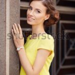 Woman in yellow dress by stone wall.