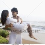 Man carrying woman on beach; romantic.