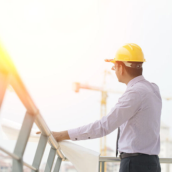 A man in yellow hard hat and tie standing next to a building.